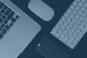 A MacBook, wireless mouse, wireless keyboard, and face down smartphone
